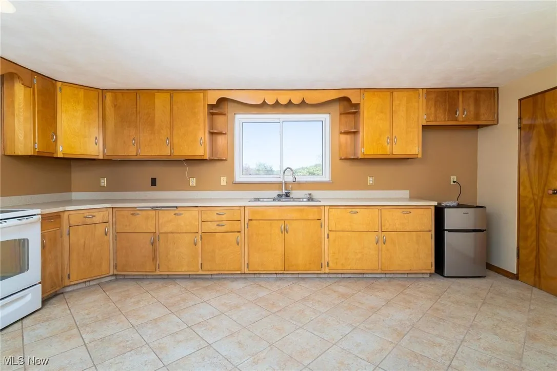 Kitchen with freestanding refrigerator, light countertops, white range with electric cooktop, brown cabinets, and light tile patterned floors
