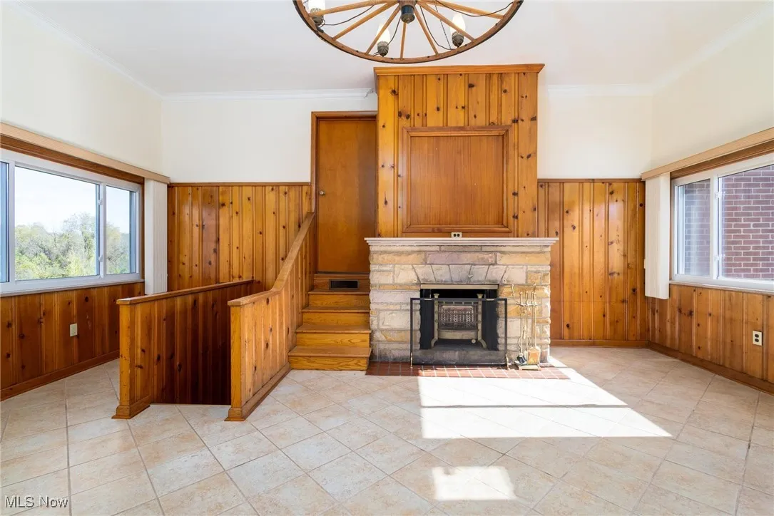 Unfurnished living room with ornamental molding, wood walls, a fireplace, stairs, and light tile patterned flooring