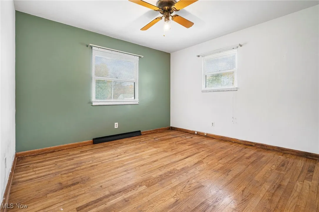 Unfurnished room featuring hardwood / wood-style flooring, baseboard heating, and a ceiling fan