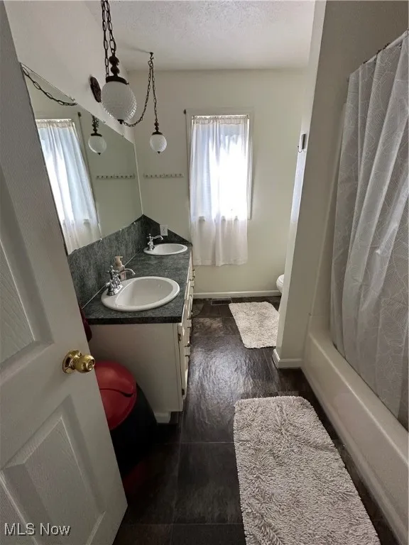 Full bathroom with double vanity, a textured ceiling, and shower / bath combo