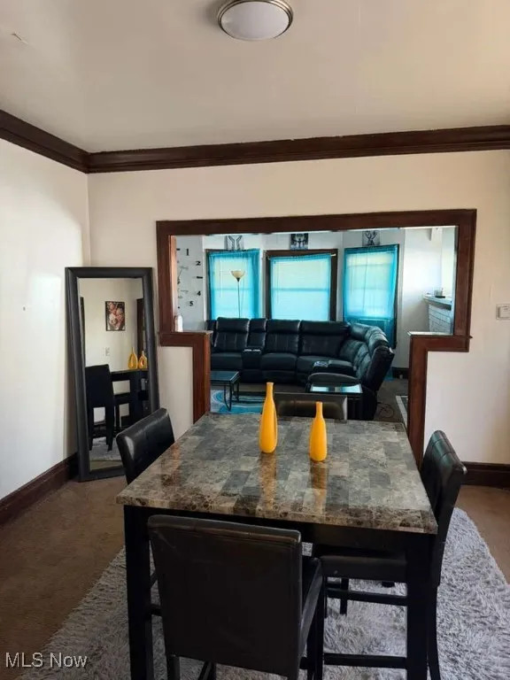 Dining room with crown molding and dark colored carpet