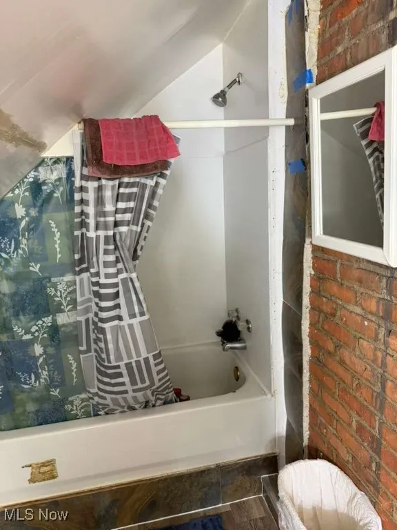 Bathroom featuring brick wall and shower / bath combo with shower curtain