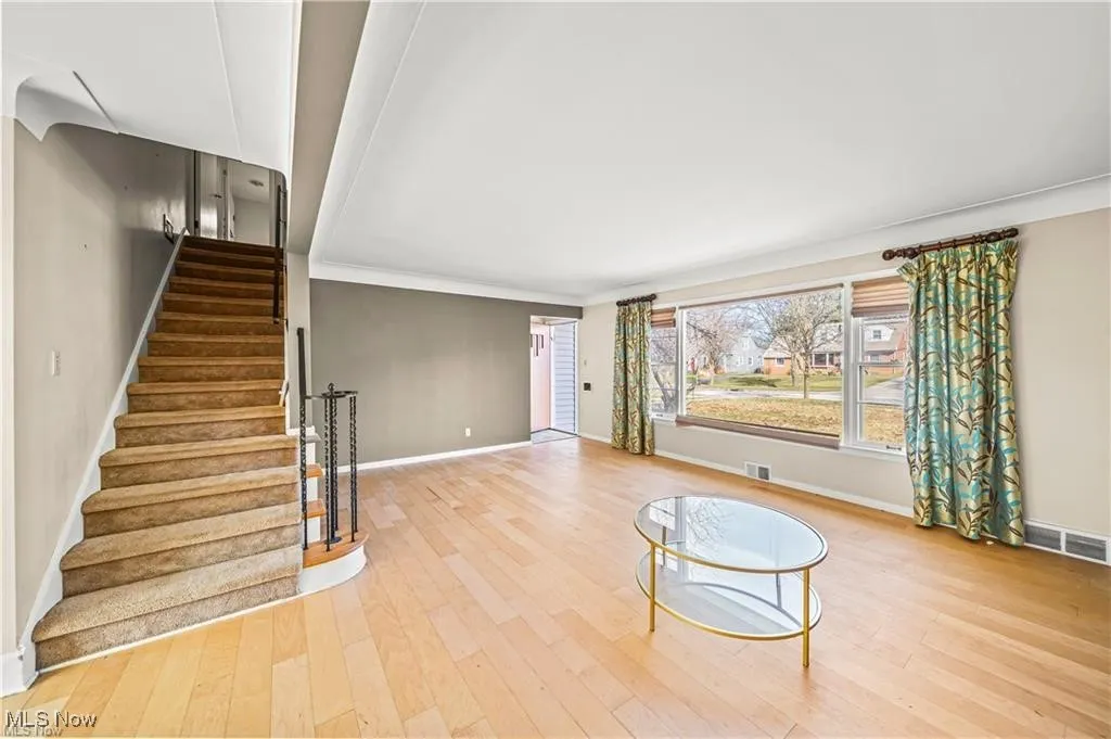 Unfurnished living room featuring light wood-style flooring, stairway, and ornamental molding
