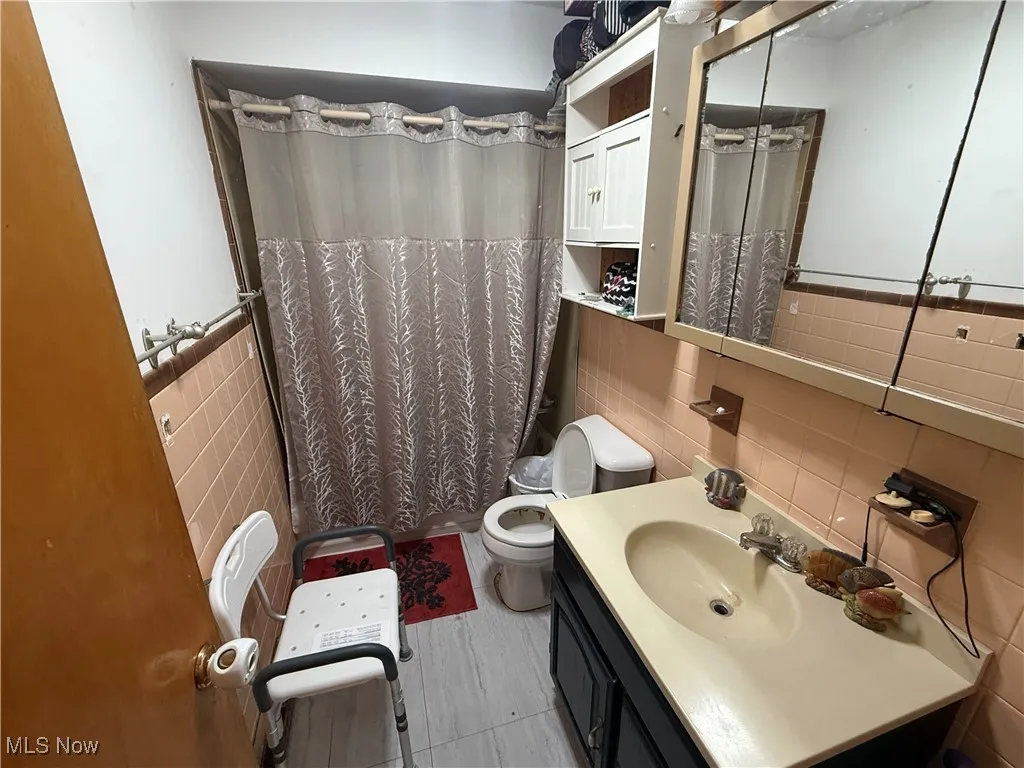 Full bath with vanity, a shower with shower curtain, and tile walls