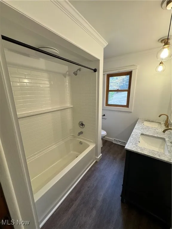 Full bath featuring shower / bath combination, double vanity, dark wood-style flooring, and ornamental molding