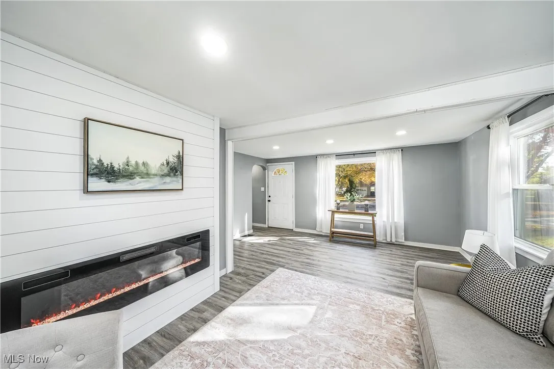 Living area with a large fireplace, recessed lighting, light wood finished floors, wood walls, and arched walkways