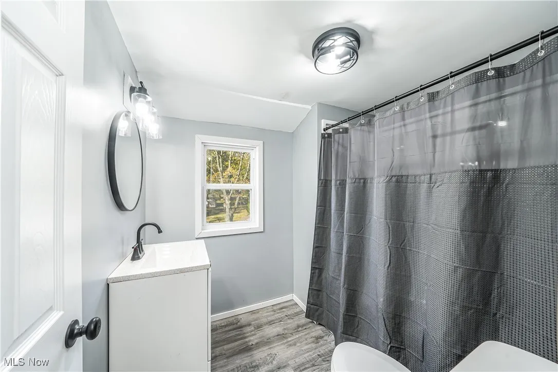 Full bath with curtained shower, vanity, and light wood-style floors