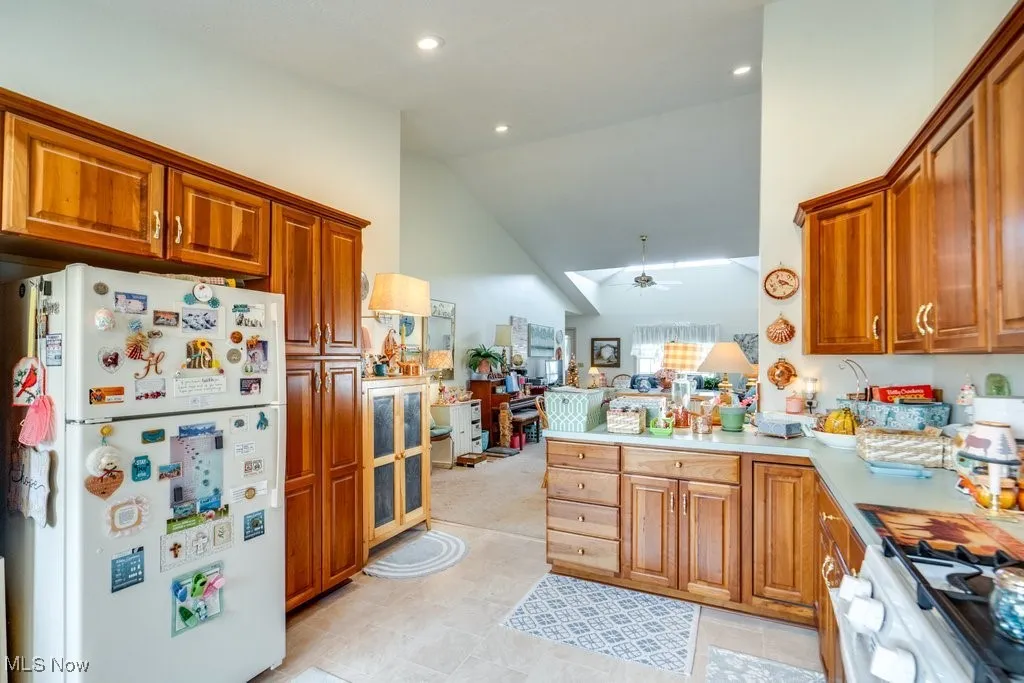 Kitchen featuring cherry cabinets, white appliances, lofted ceiling, light countertops, and a peninsula