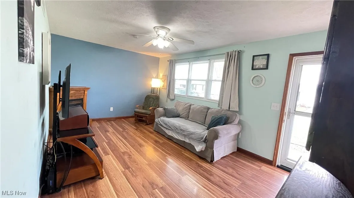 Living room featuring light wood-style floors, a textured ceiling, and a ceiling fan