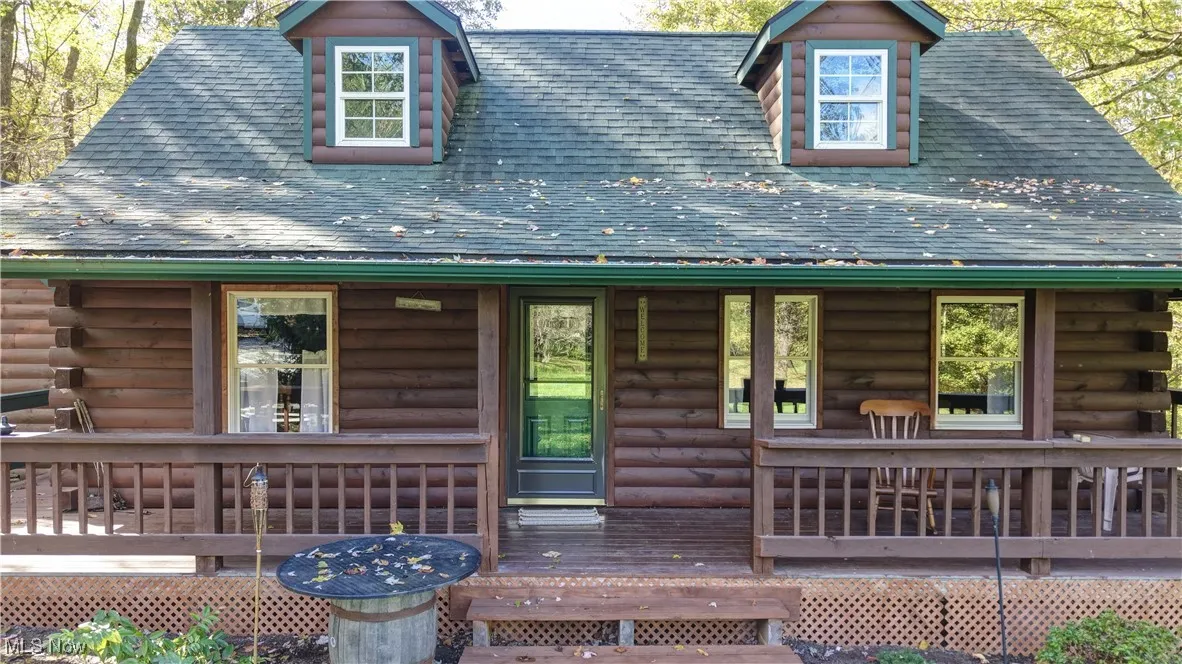 Doorway to property featuring a shingled roof, log exterior, and a deck