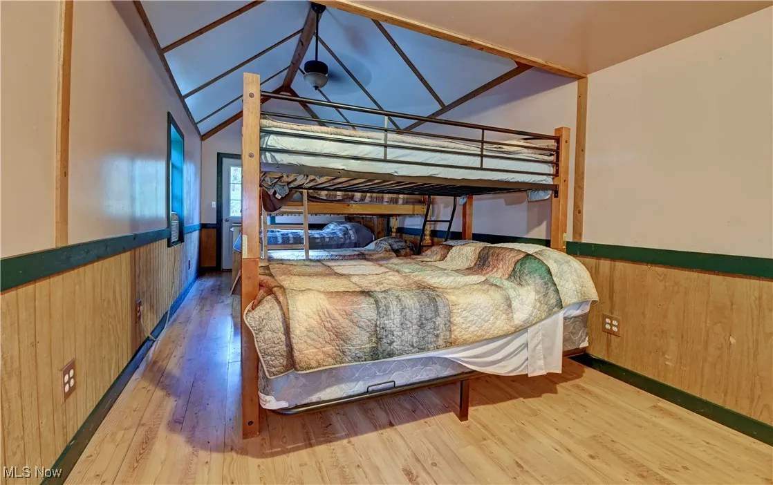 Bedroom featuring wooden walls, wainscoting, hardwood / wood-style floors, and vaulted ceiling