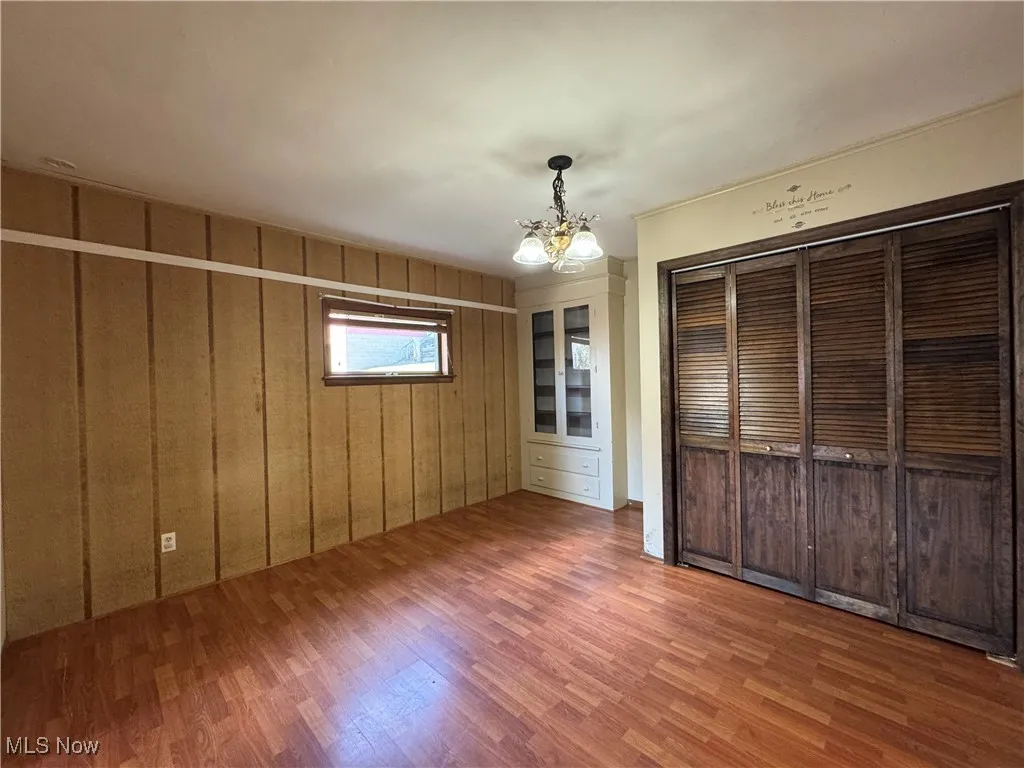 Unfurnished bedroom featuring wood finished floors, a closet, a chandelier, and wooden walls