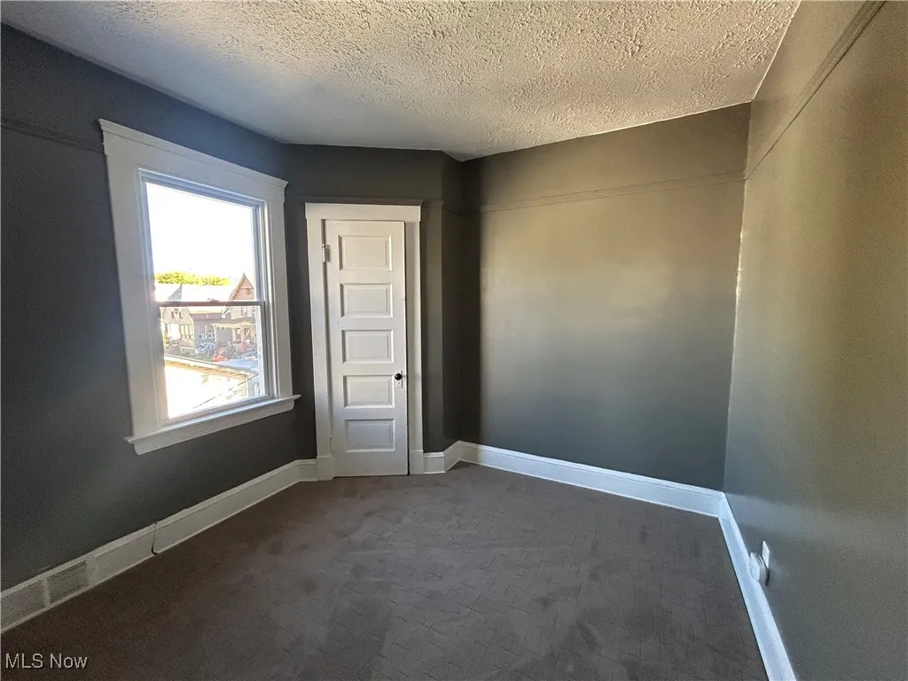 Unfurnished room featuring a textured ceiling and dark carpet