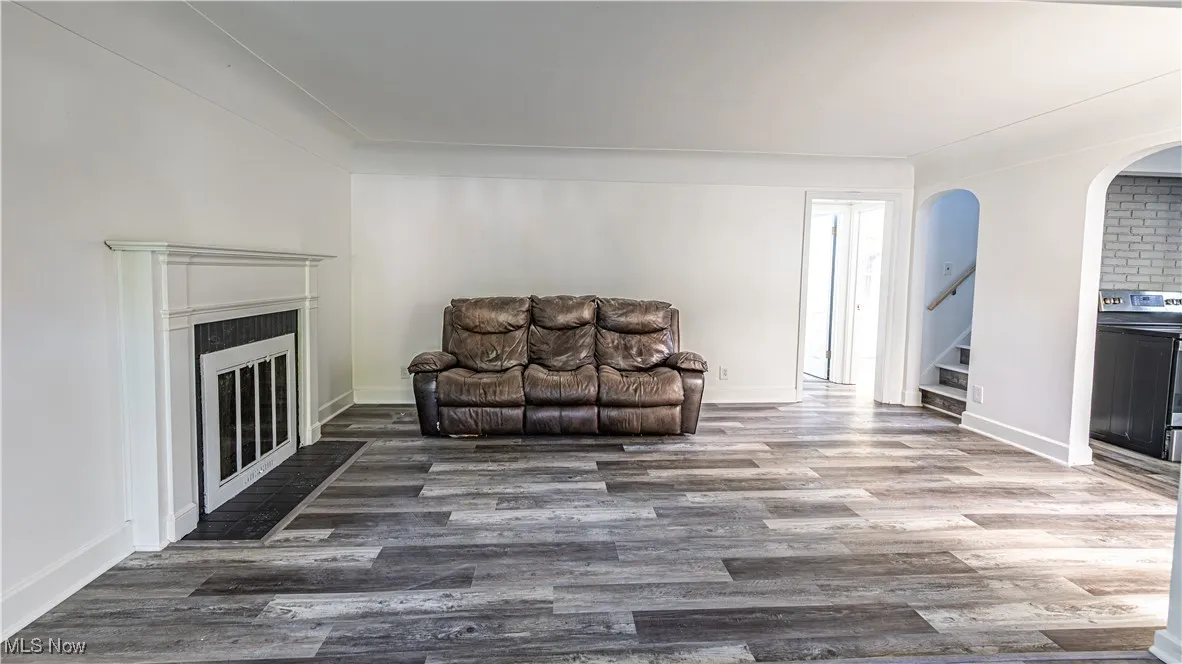 Living area featuring arched walkways, a glass covered fireplace, wood finished floors, and stairs