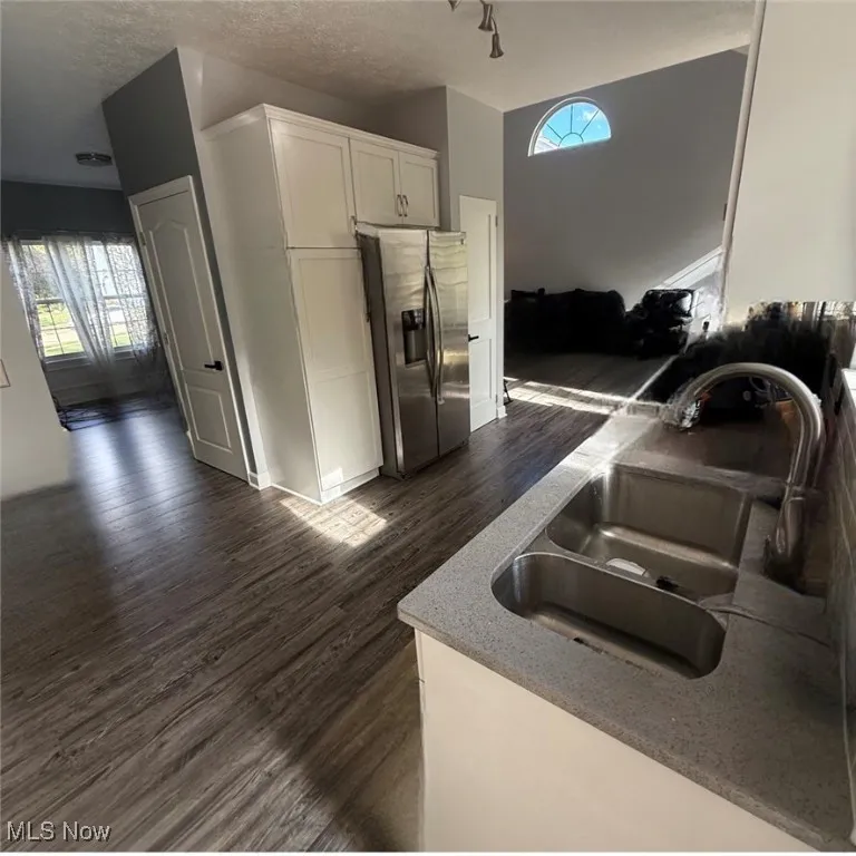 Kitchen featuring white cabinets, stainless steel refrigerator with ice dispenser, dark wood-style floors, and a textured ceiling