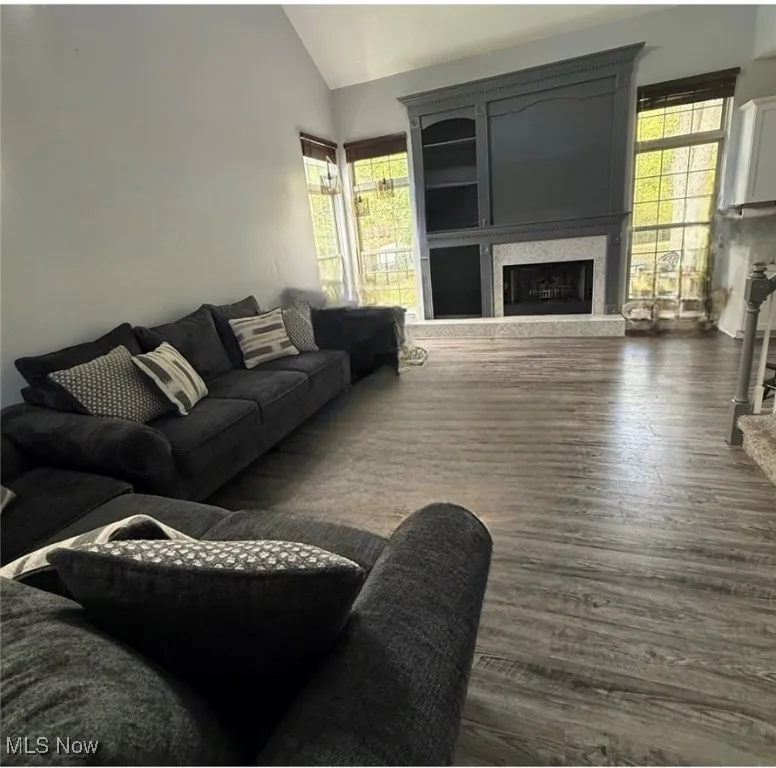 Living room with a fireplace, dark wood-style flooring, and lofted ceiling