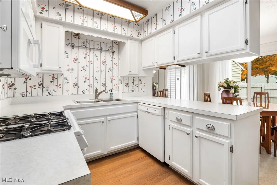 Kitchen featuring light countertops, white cabinets, white appliances, a peninsula, and wallpapered walls