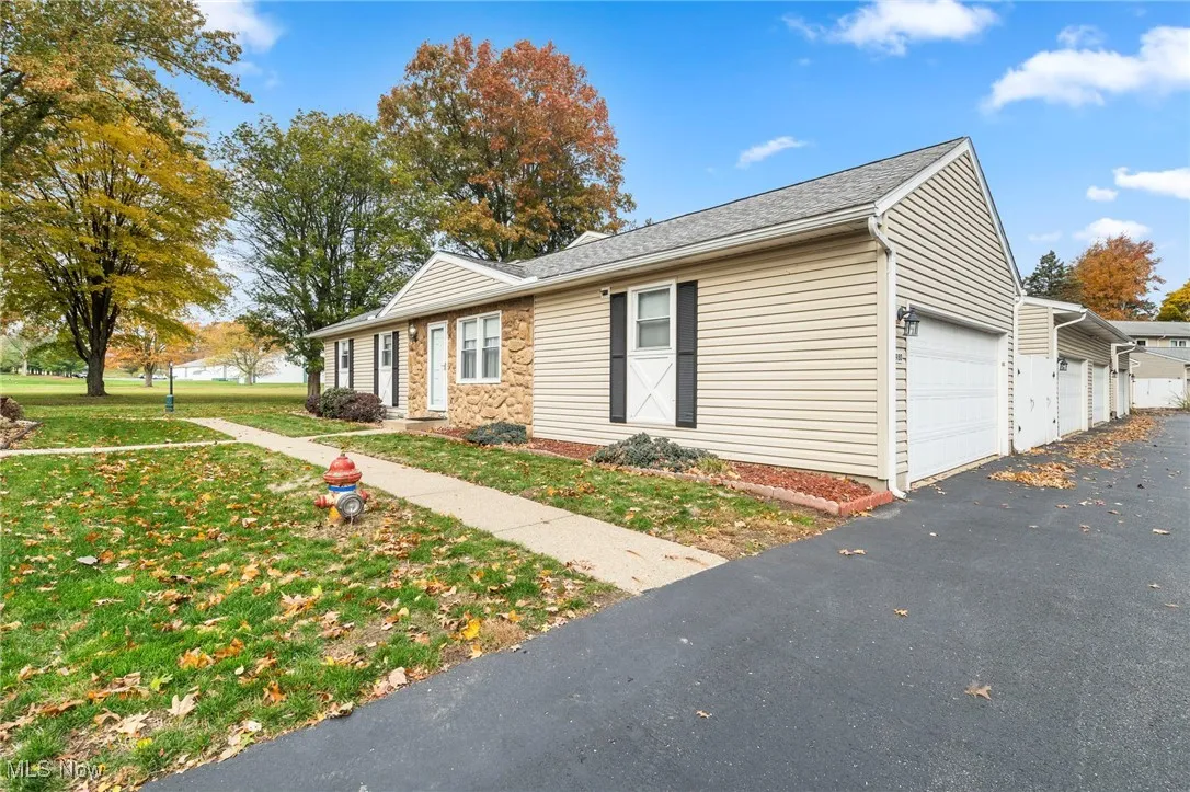 View of front of property featuring a garage, a front lawn, stone siding, and roof with shingles