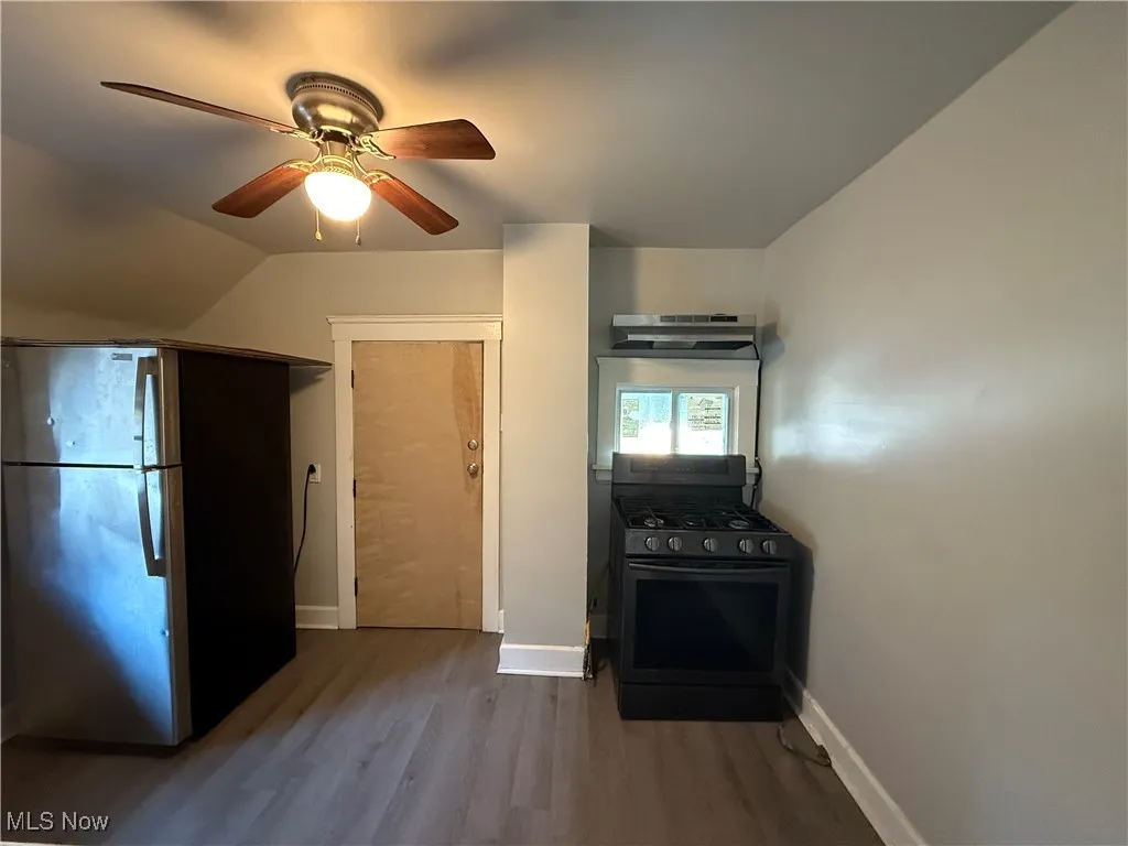 Kitchen with freestanding refrigerator, gas range, dark wood-type flooring, a ceiling fan, and lofted ceiling