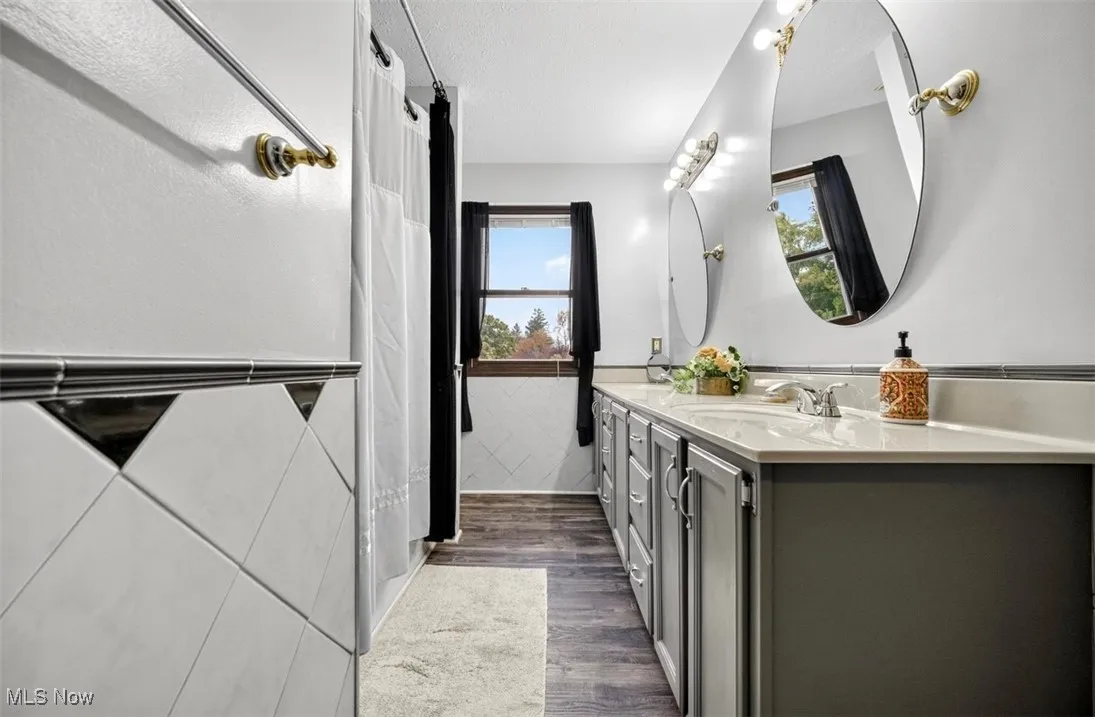 Full bathroom with double vanity, dark wood-style flooring, and curtained shower