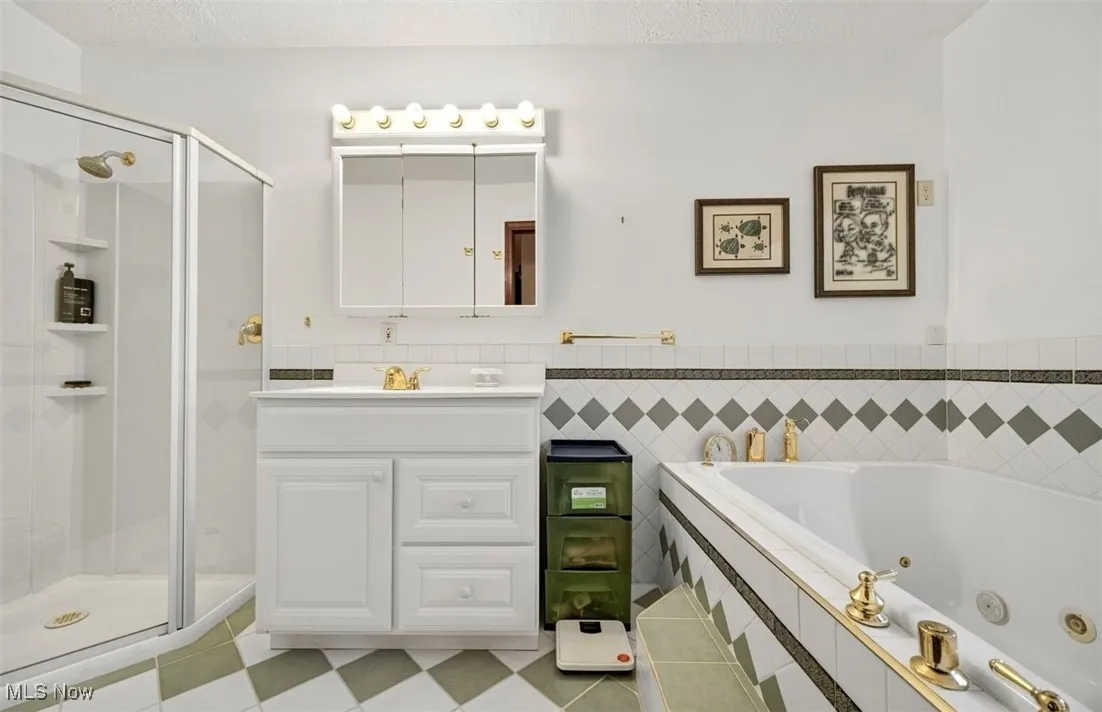 Full bathroom with vanity, a shower stall, a whirlpool tub, and tile walls