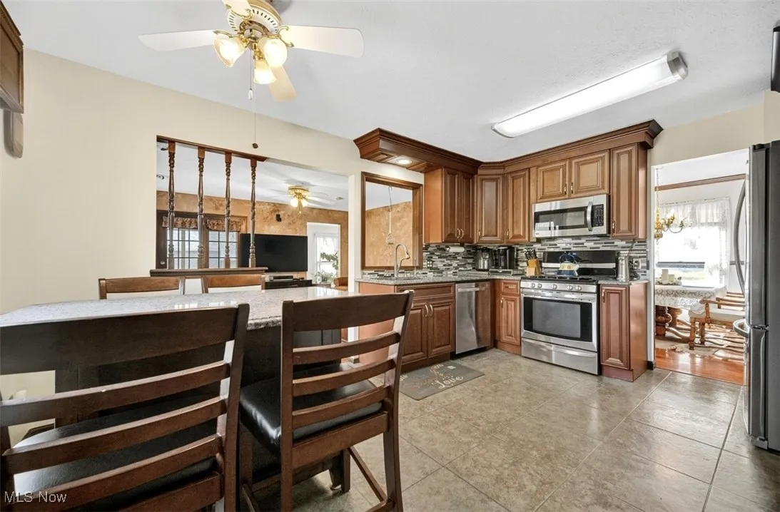 Kitchen with appliances with stainless steel finishes, tasteful backsplash, light stone countertops, and brown cabinetry