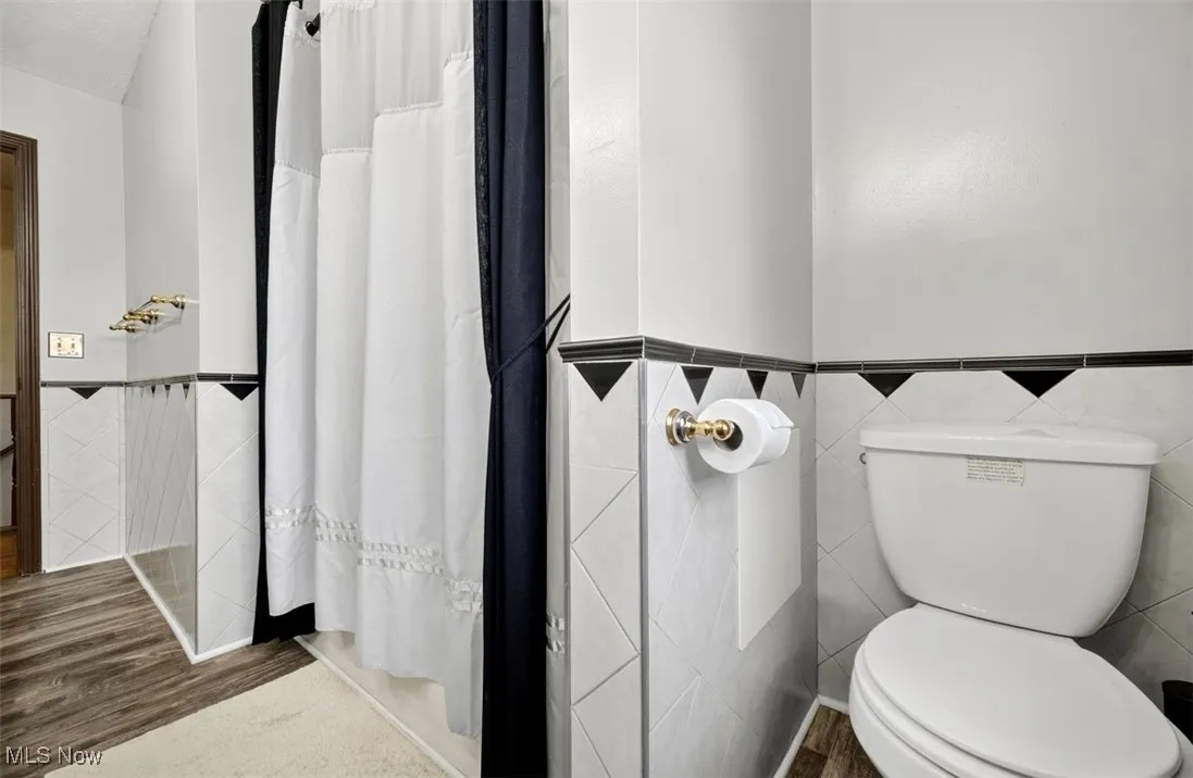 Bathroom with tile walls, a shower with shower curtain, wainscoting, and wood finished floors
