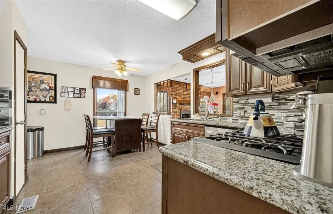 Kitchen with decorative backsplash, extractor fan, light stone countertops, light tile patterned floors, and a ceiling fan