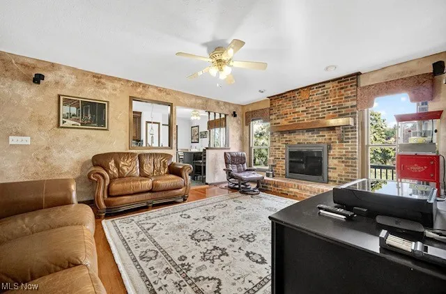 Living room with plenty of natural light, a fireplace, a ceiling fan, a textured wall, and wood finished floors