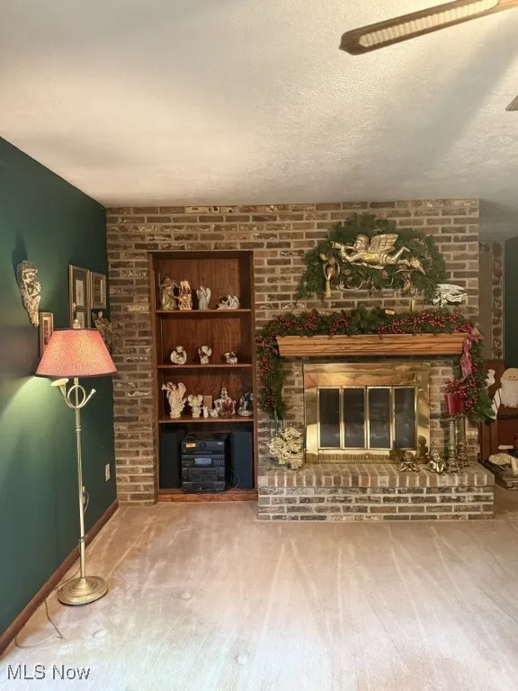 Carpeted living area featuring brick wall, a textured ceiling, a brick fireplace, and a ceiling fan