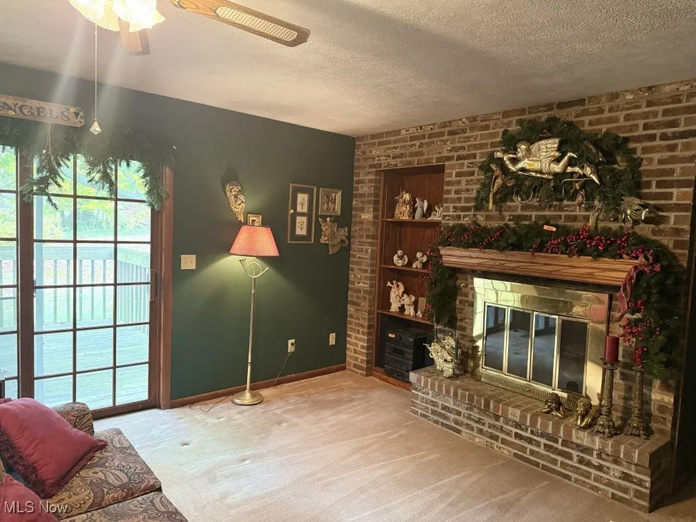 Living room featuring a textured ceiling, brick wall, carpet floors, and a brick fireplace