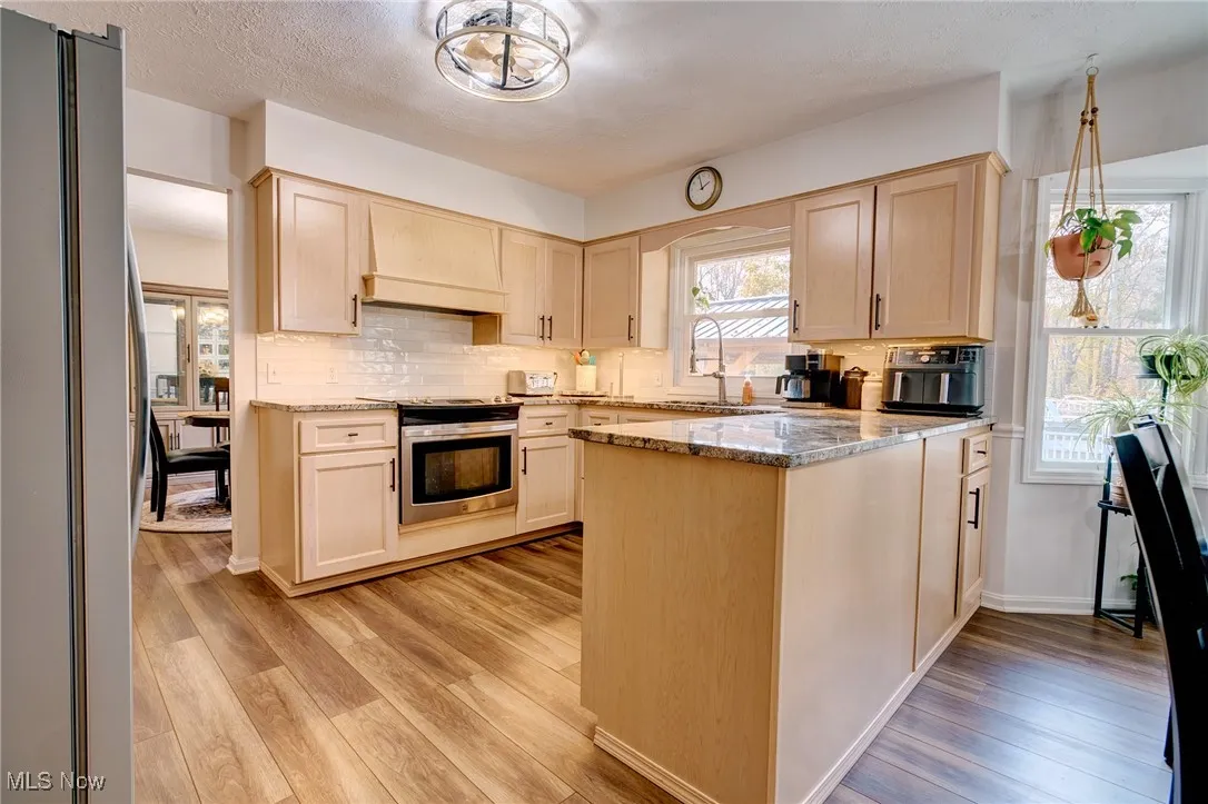 Kitchen with light stone counters, freestanding refrigerator, decorative backsplash, a peninsula, and light wood-style flooring