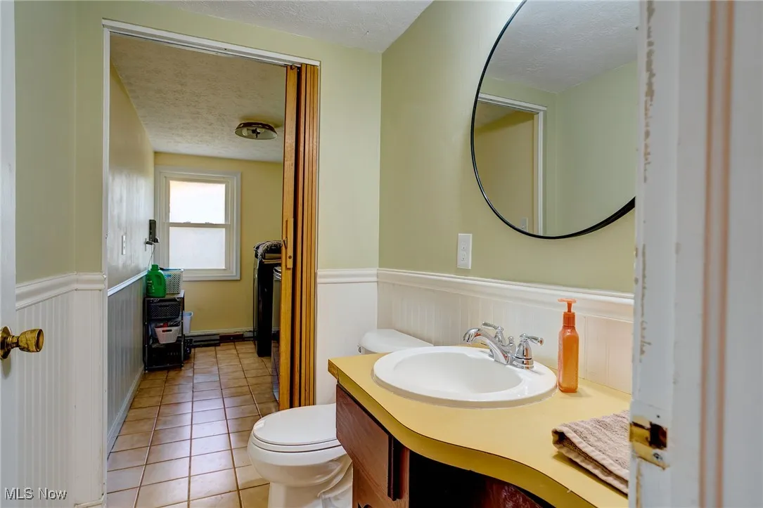 Half bathroom with light tile patterned flooring, a textured ceiling, vanity, and wainscoting