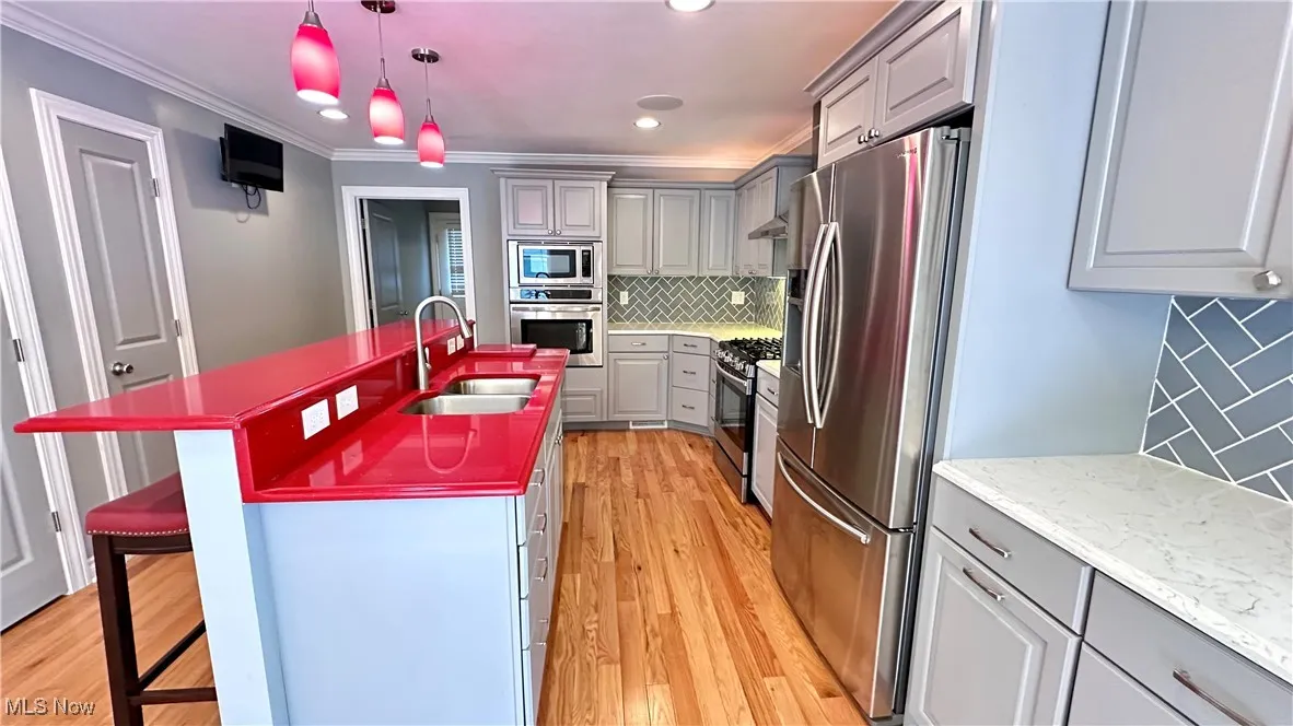 Kitchen with gray cabinets, stainless steel appliances, tasteful backsplash, a kitchen breakfast bar, and light wood-type flooring