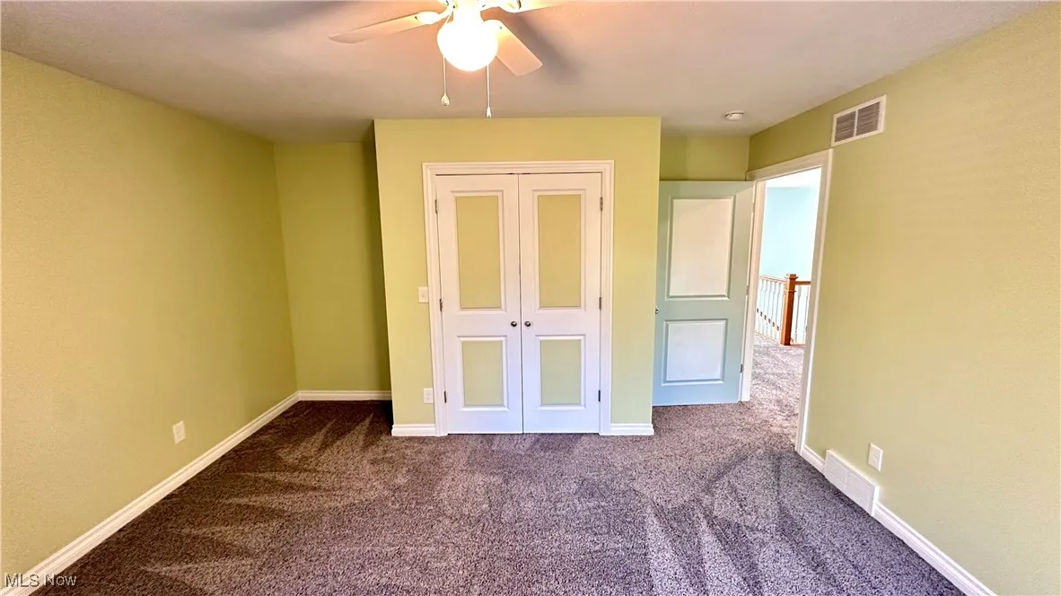 Unfurnished bedroom featuring dark colored carpet, a ceiling fan, and a closet