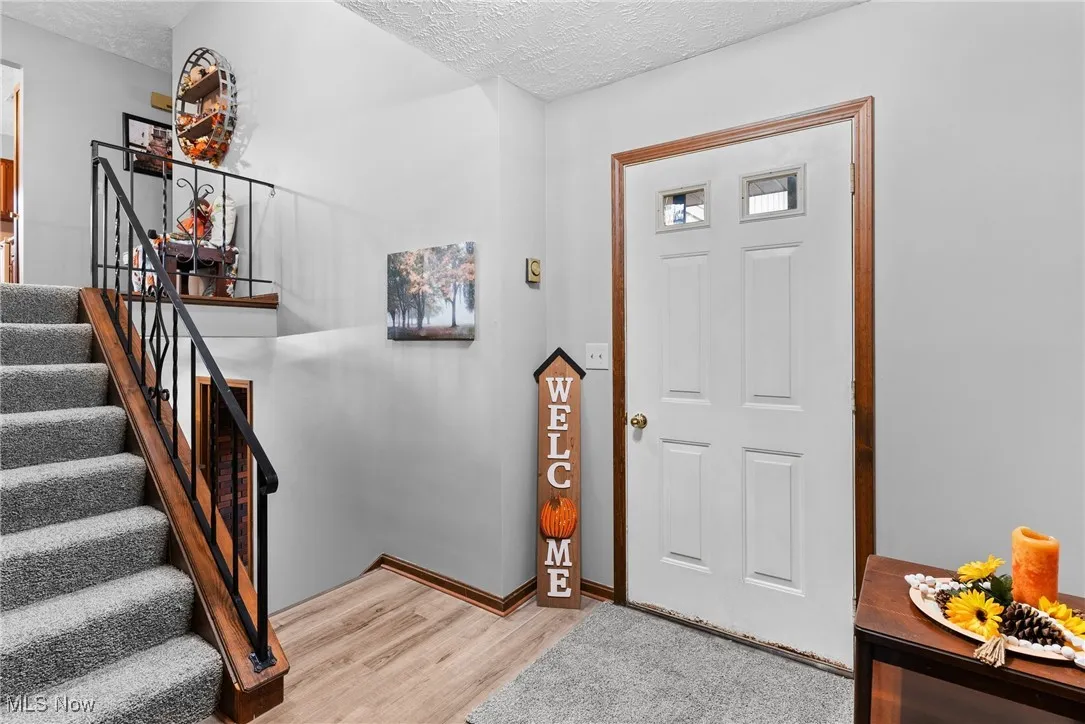 Entrance foyer featuring stairs, light wood finished floors, and a textured ceiling