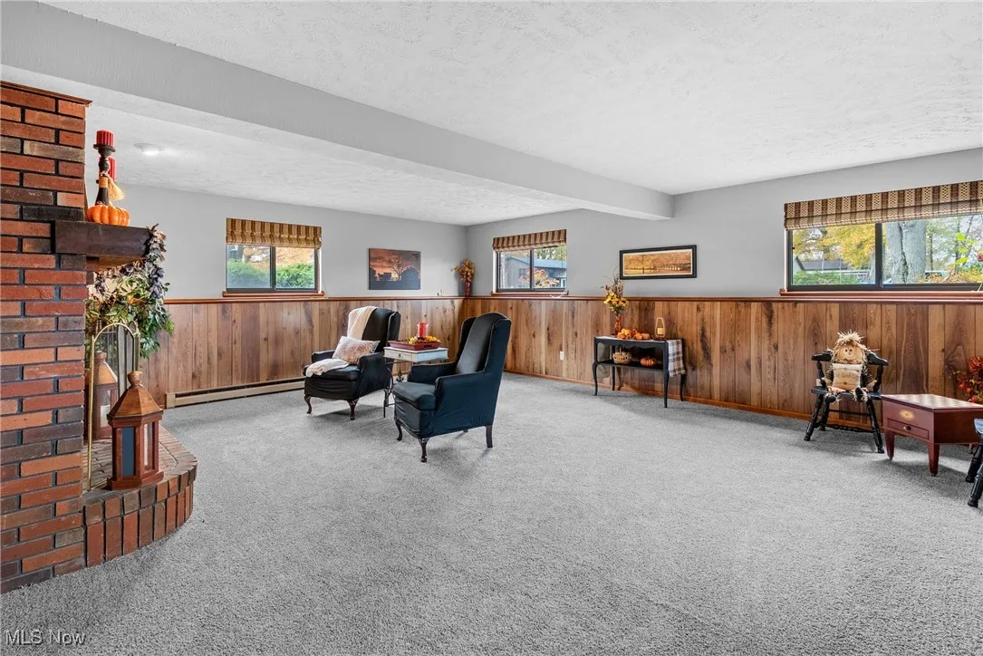 Sitting room featuring a textured ceiling, wood walls, carpet floors, wainscoting, and a baseboard radiator