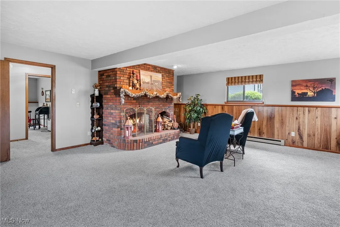 Carpeted living area with wood walls, a fireplace, a textured ceiling, a baseboard heating unit, and a wainscoted wall