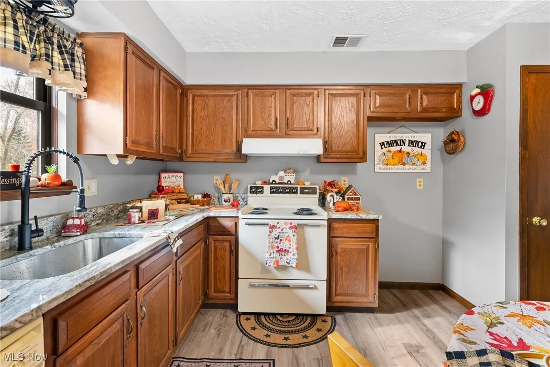 Kitchen featuring white electric range oven, brown cabinetry, light wood-style flooring, a textured ceiling, and light stone counters