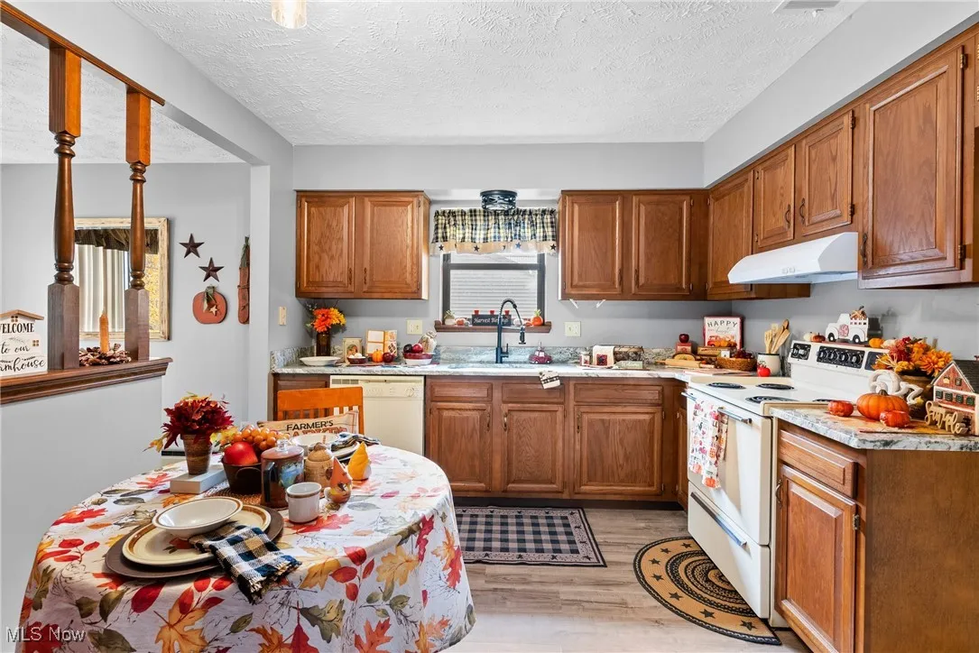 Kitchen featuring white appliances, brown cabinetry, a textured ceiling, light countertops, and light wood finished floors