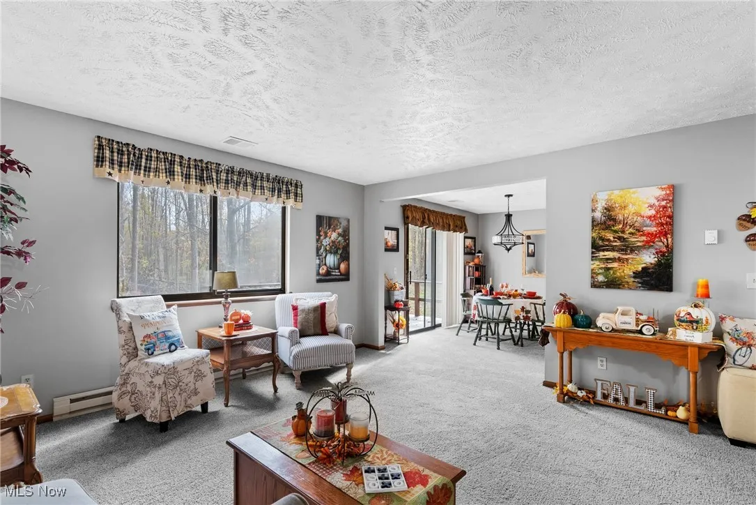 Living room featuring carpet flooring, baseboard heating, a textured ceiling, and a chandelier