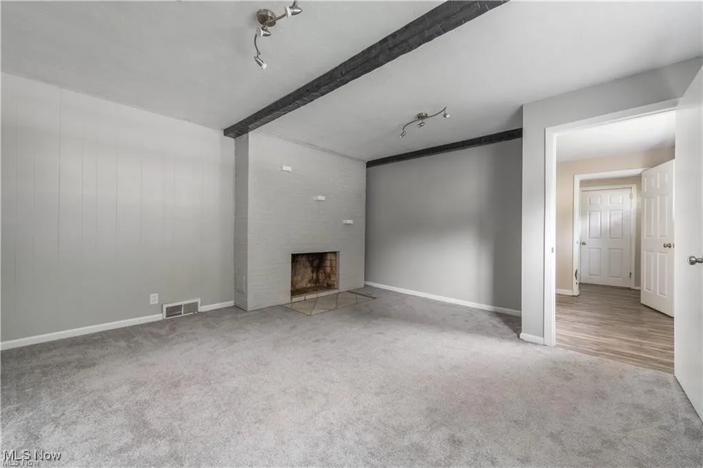 Unfurnished living room with light colored carpet, a brick fireplace, beamed ceiling, and rail lighting