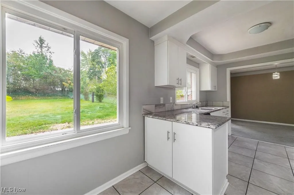 Kitchen with white cabinets, light tile patterned flooring, light stone counters, and a peninsula