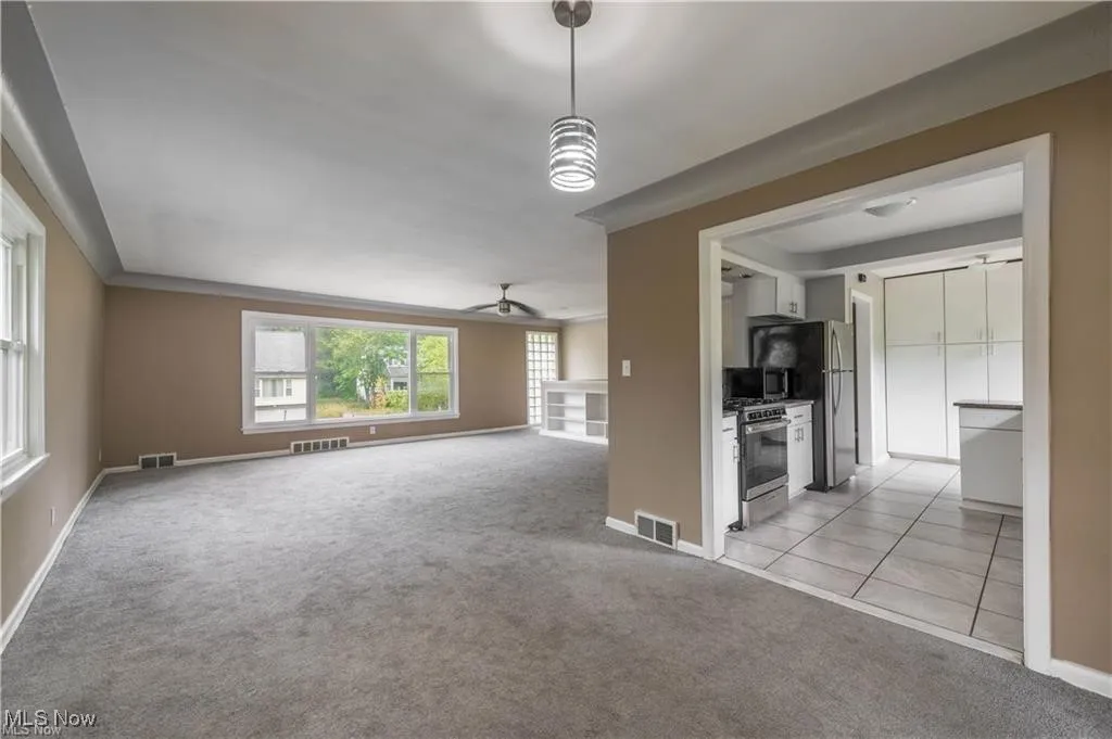 Unfurnished living room with light colored carpet, a ceiling fan, a fireplace, and light tile patterned flooring