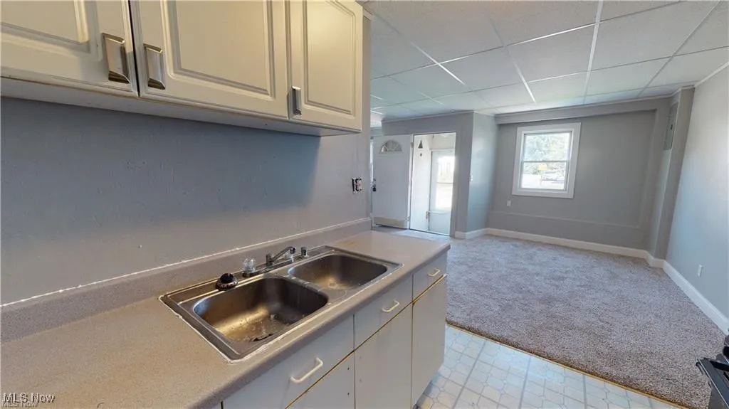 Kitchen with light countertops, a drop ceiling, light carpet, open floor plan, and white cabinetry