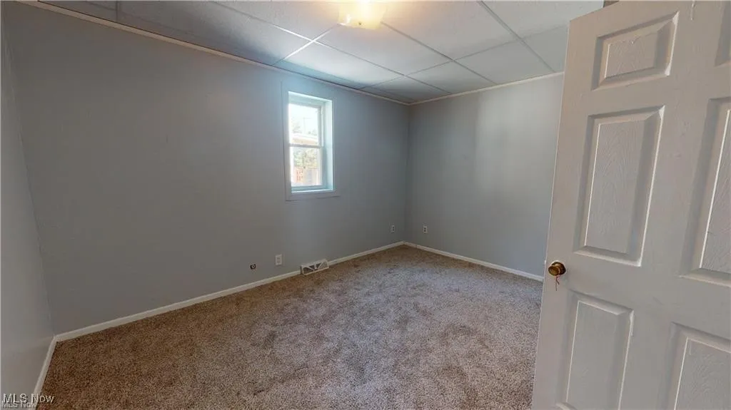 Carpeted spare room featuring baseboards and a paneled ceiling