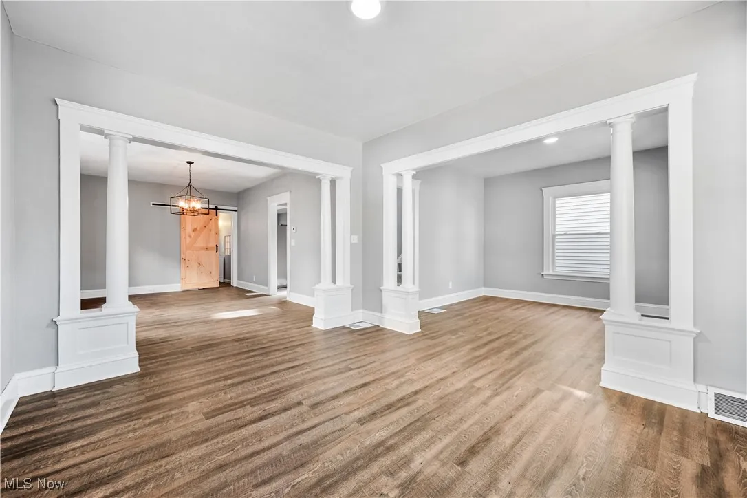 Unfurnished living room featuring ornate columns, a chandelier, wood finished floors, a barn door, and recessed lighting