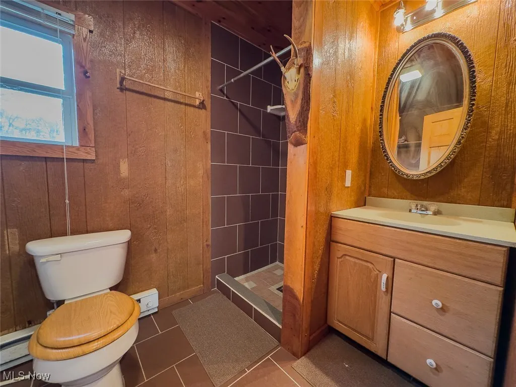 Full bath with wooden walls, vanity, a stall shower, dark tile patterned floors, and a baseboard heating unit