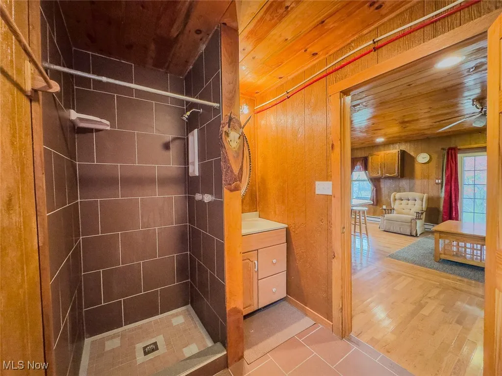 Full bath featuring a shower stall, light tile patterned floors, vanity, wooden ceiling, and wood walls