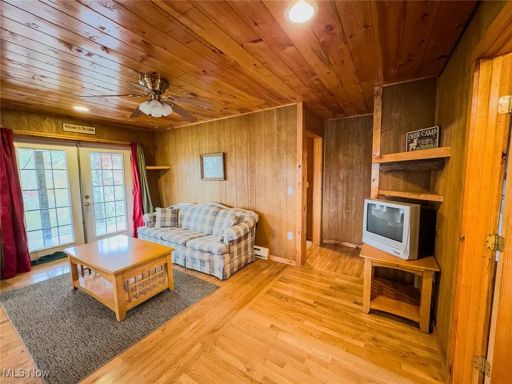 Living room with light wood-type flooring, french doors, wooden ceiling, wooden walls, and a ceiling fan